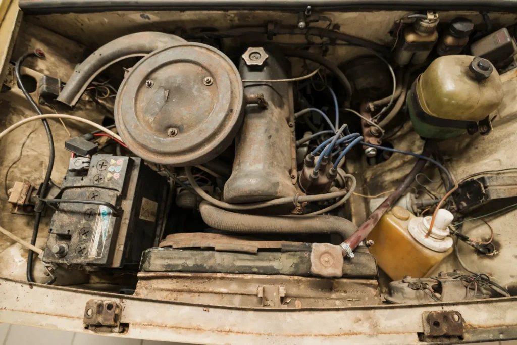 Detail starého a znečištěného motorového prostoru automobilu s viditelnými kabely a baterií.